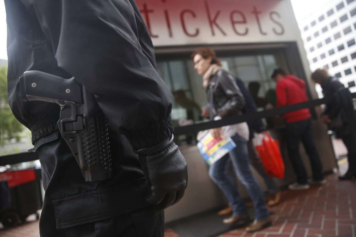 Kasayle Howard (left), armed security guard with Cypress Security, stands next to the cable car fare kiosk while working at Powell and Market Streets as people purchase tickets on Monday, April 20, 2015 in San Francisco, Calif.