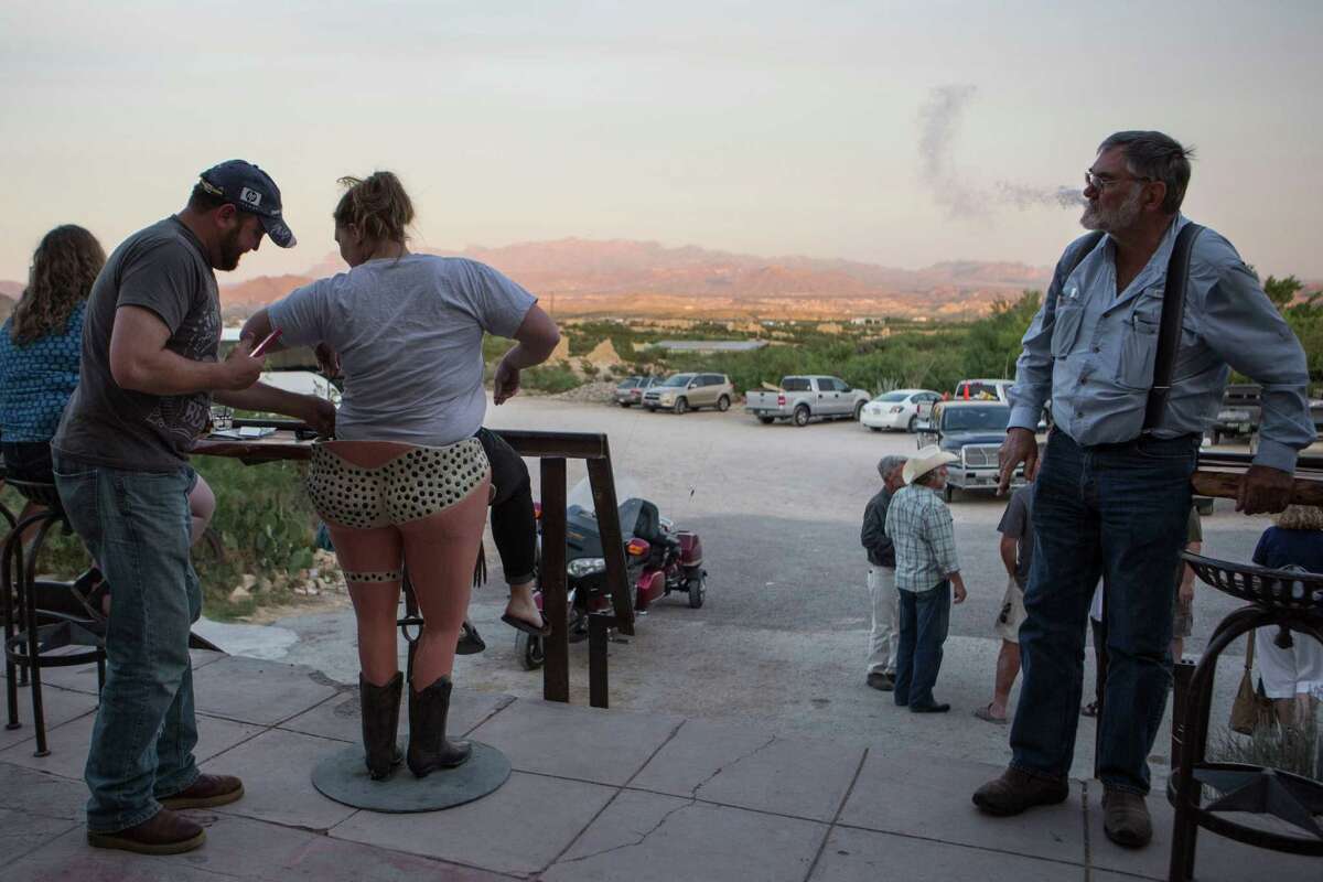 Robert Krull, right, looks on as Wayne Brown, left, helps Tomi Hutton get onto a stool on the porch of the Starlight Theatre before taking her picture on April 20, 2015 in Terlingua, TX . Both were visiting from Dallas. Hutton said, "We are just here having a good time."
