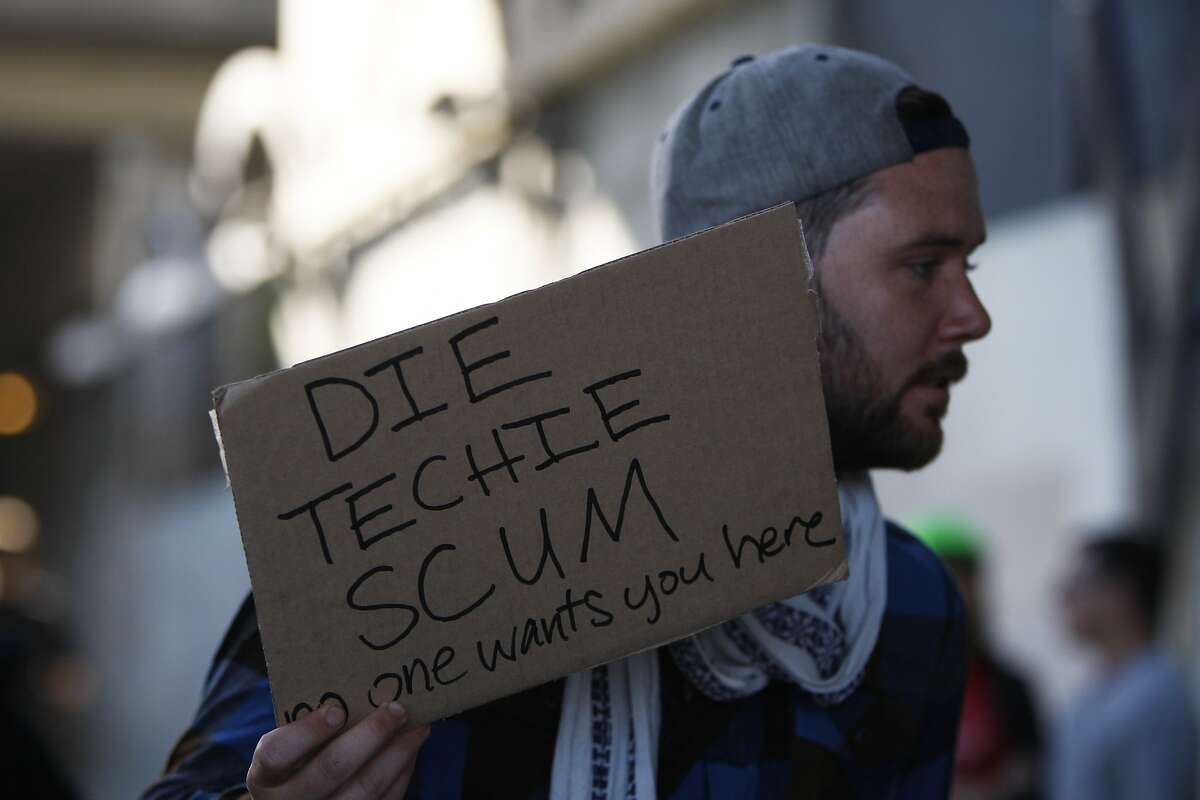 A man holds a sign during a protest organized to block tech commuter buses outside MacArthur BART station in Oakland, Calif. Friday, May 1, 2015.