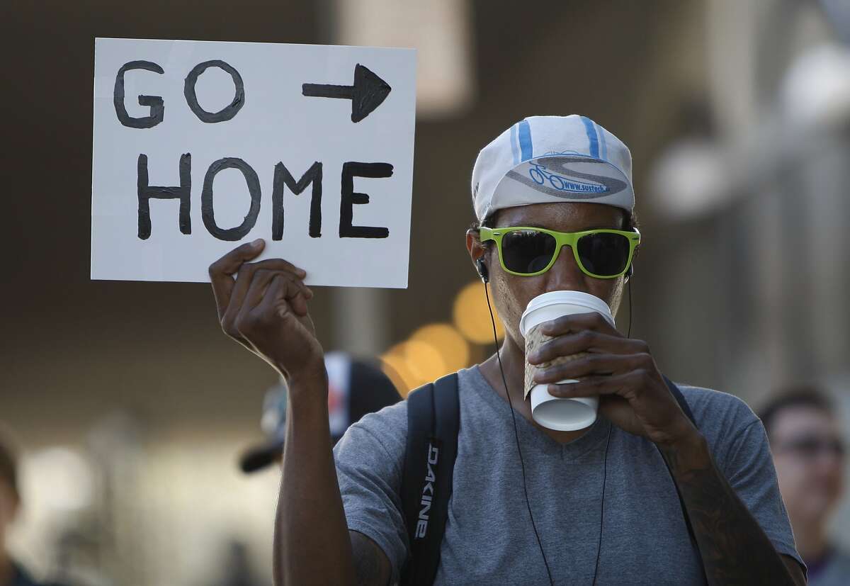 A demonstrator by the name of T.J. holds a sign that reads "Go Home" during a morning protest organized to block tech commuter buses outside MacArthur BART station in Oakland, Calif. Friday, May 1, 2015.