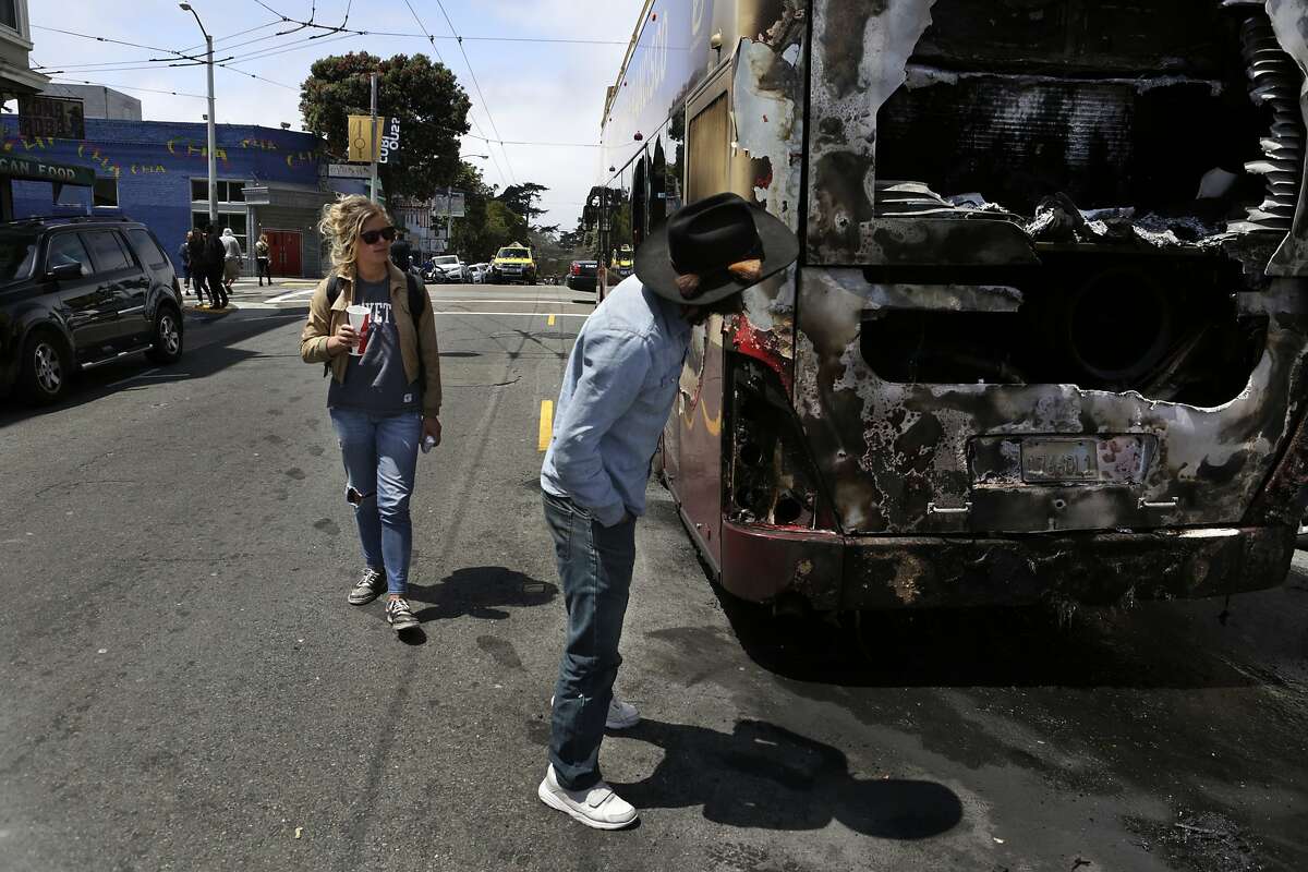 Passersby look at a tourist bus that caught fire at the intersection of Haight and Shrader streets in San Francisco on Sunday, May 3, 2015.