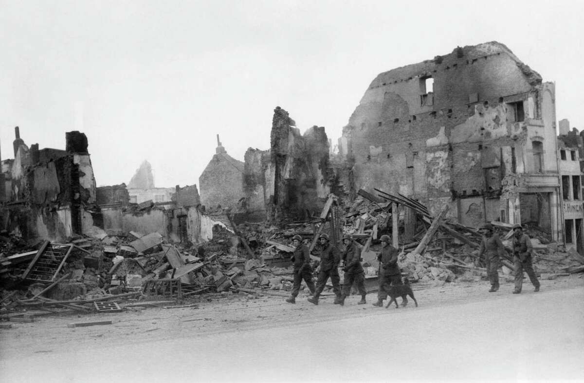 American soldiers walk through a street in war-torn Bastogne, Belgium on Dec. 13, 1945 after the Yanks relieved the divisions trapped there for a week during the German breakthrough in the Belgium-Luxembourg salient in December 1944. Wrecked buildings were caused by shelling and bombing, Bastogne is quiet and peaceful and the stillness is only broken by an occasional transport plane passing overhead or the blows of hammers in repair jobs. (AP Photo/B.H. Rollins )