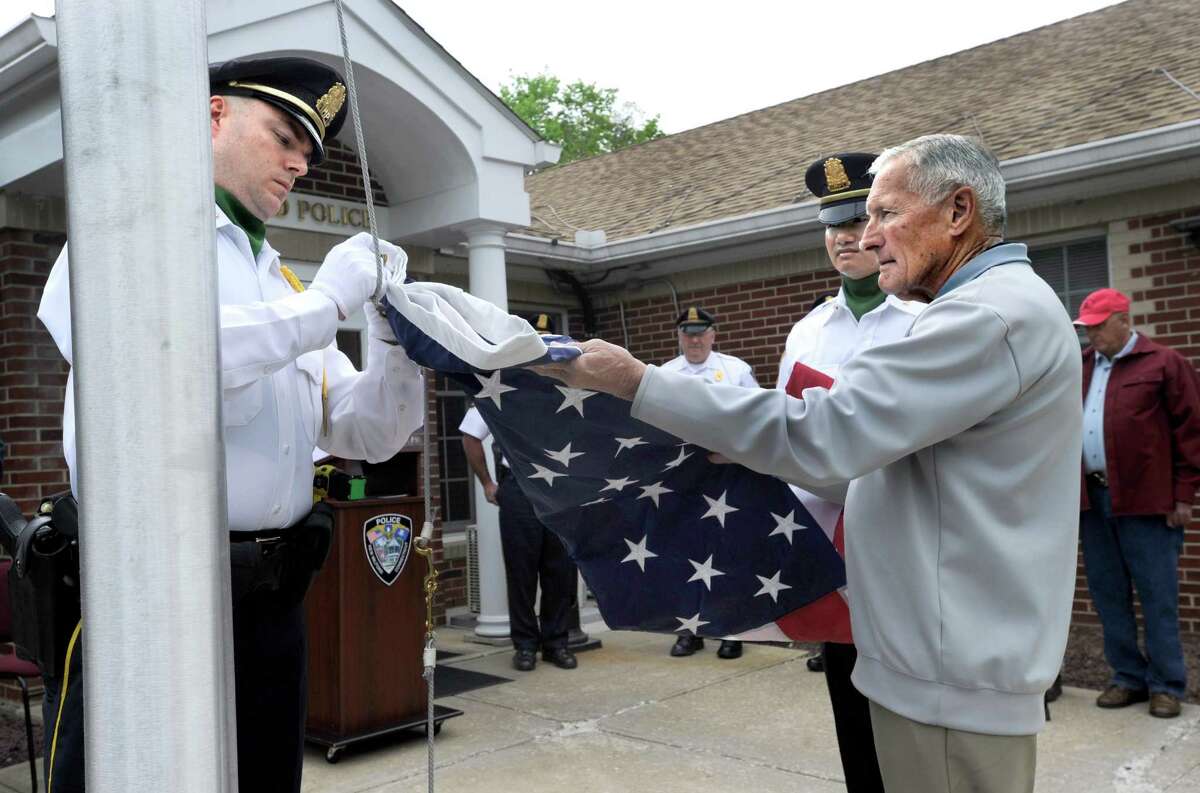 Sgt. Ed Hannan, left, and Officer Dru Sin, part of an Honor Guard, and Larry Couch, a nephew, unfold and hook an American flag to raise on a new flag poll that is part of the memorial to the late New Milford Police Office H. Kenneth Couch. New Milford Police Officer H. Kenneth Couch who died during a water rescue in the Housatonic River on June 3, 1964, is remembered with a memorial monument and plaque during a ceremony at the New Milford Police Station Friday, May 15, 2015.