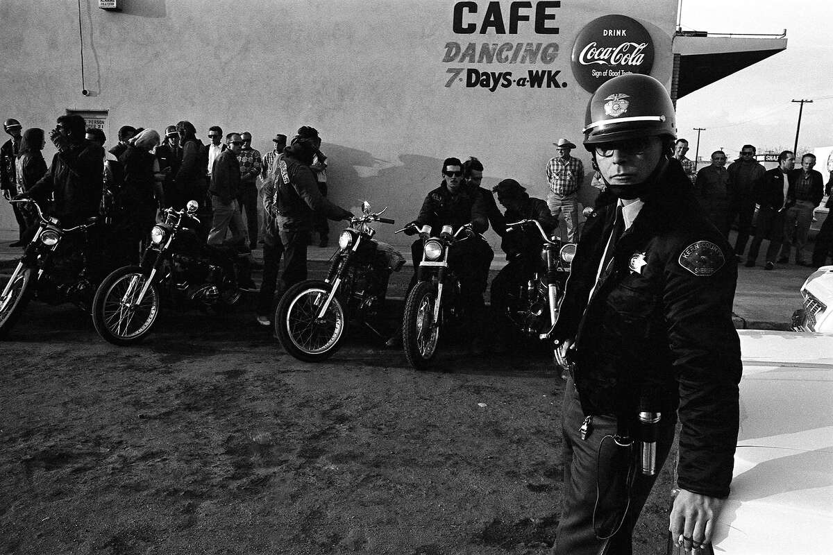 As the sun sets outside a bar that the Hells Angels have, in effect, made their headquarters-away-from-home during their San Bernardino-to-Bakersfield run, a sheriff's deputy keeps an eye on the proceedings in 1965.