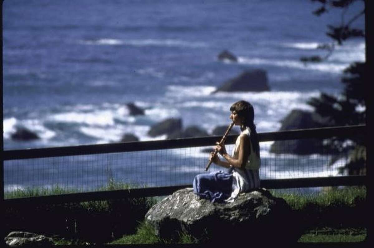 A woman sitting on a rock, playing a wooden flute, on the cliffs overlooking the Pacific Ocean at the Esalen Institute in Big Sur, Calif., on April 1, 1987.