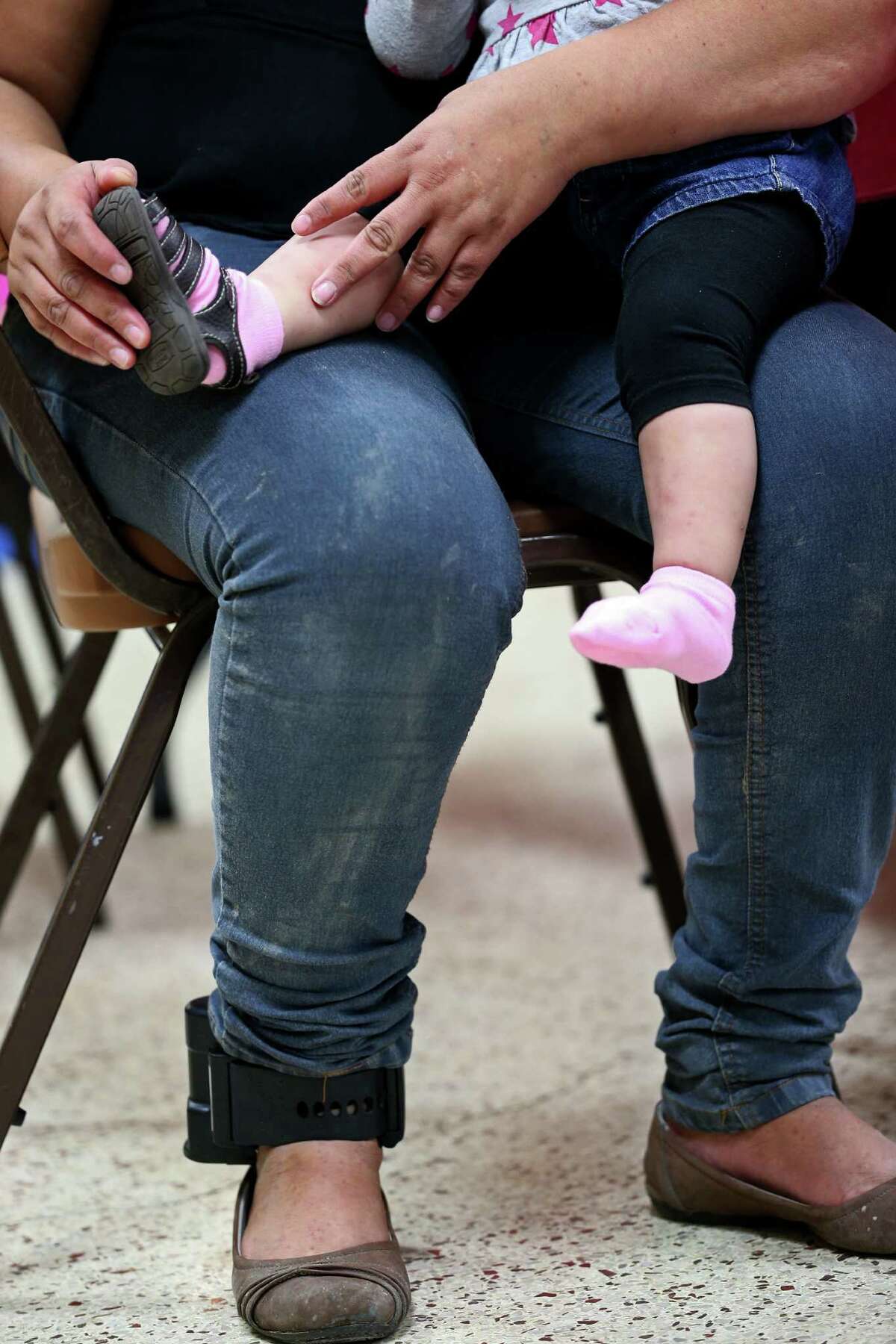 A Central American immigrant wears an ankle monitor while trying shoes on her infant daughter at the Sacred Heart Catholic Church shelter, Thursday, May 21, 2015. According to volunteers, they started noticing adult immigrants with the monitors, provided by U.S. Customs and Immigration Enforcement, on May 13. After they are processed by immigration, some of the immigrants are released on their own recognizance with a date to appear before an immigration judge at the arrival destination in the US. The monitors are used to insure that they show up before a judge according to an immigration statement.