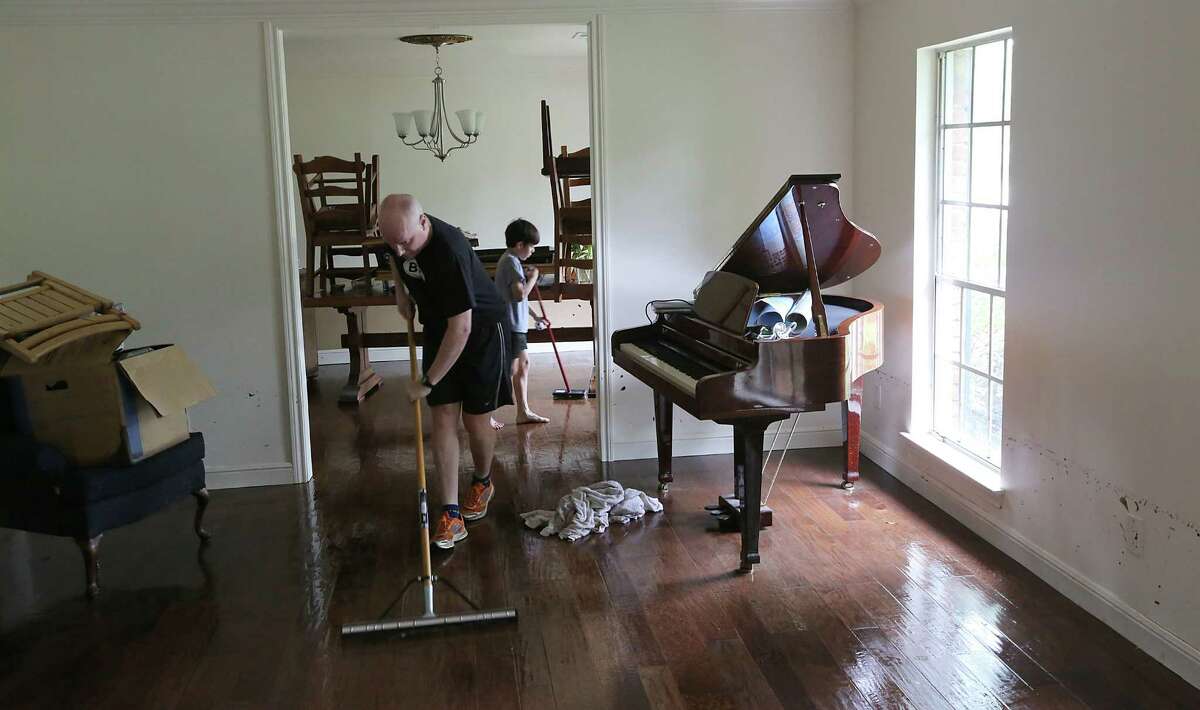 Alex Weisbach mops water while Gabriel Varon sweeps water from the hardwood floors at 5307 S. Braeswood on Tuesday, May 26, 2015 in Houston, TX The storm brought in two feet of water in their house and knocked down a tree in the front yard.On the right you can see the water mark on the wall. (Photo: Thomas B. Shea/For the Chronicle)