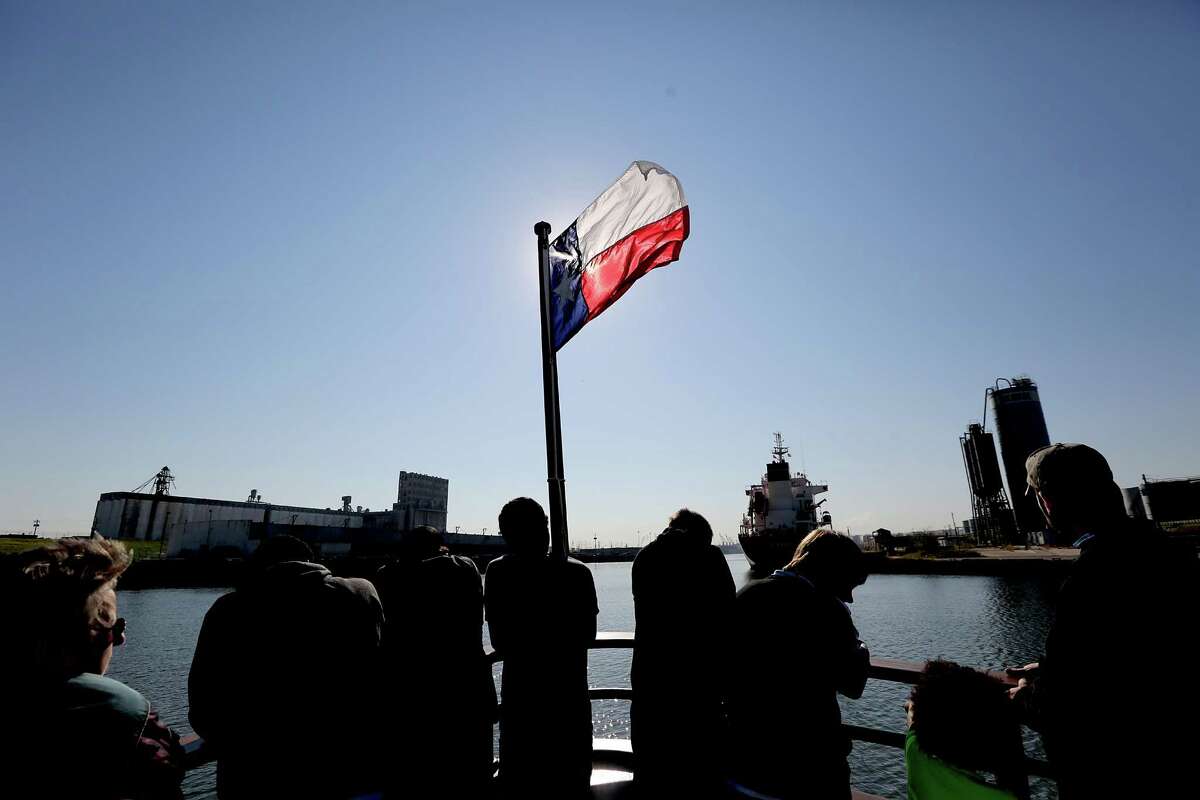 Passengers stand on the bow of the ship as the Texas flag is silhouetted as the Sam Houston travels the Houston Ship Channel on October 24, 2014 in Houston, TX. The Sam Houston offers a free 90 minute round trip cruise along the Houston Ship Channel. Embarking from the port's Sam Houston Pavilion, visiting sightseers aboard the M/V Sam Houston can enjoy passing views of international cargo vessels, and operations at the port's Turning Basin Terminal. The 95-ft. vessel holds up to 90 passengers and features air-conditioned lounge seating as well as standing room outside on the boat's deck.