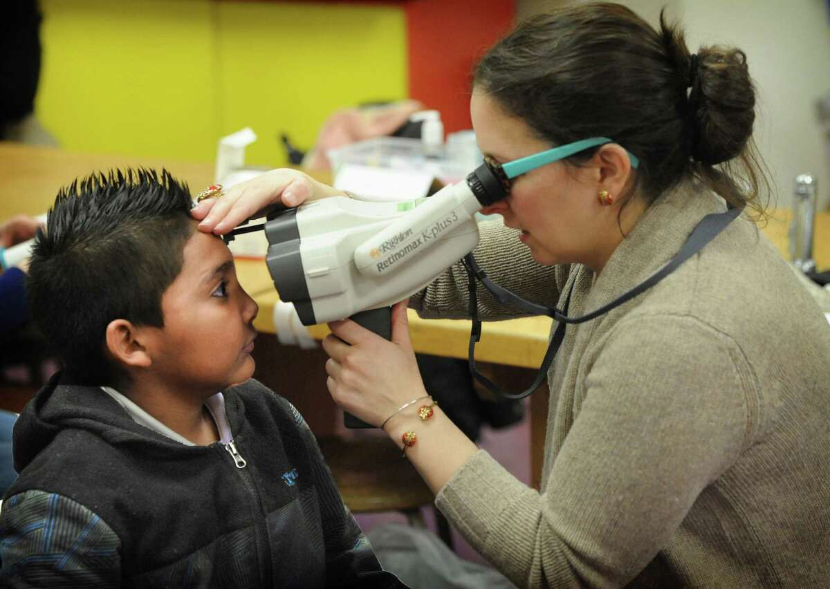 Ellen Marcus, a research assistant and a student at Johns Hopkins University, helps second-grader Anthony Martinez, 7, try on frames. Dr. Megan Collins gave Anthony a vision screening as part of the Baltimore Reading and Eye Disease Study, which seeks to discover if reading difficulties are tied to poor vision. ﻿
