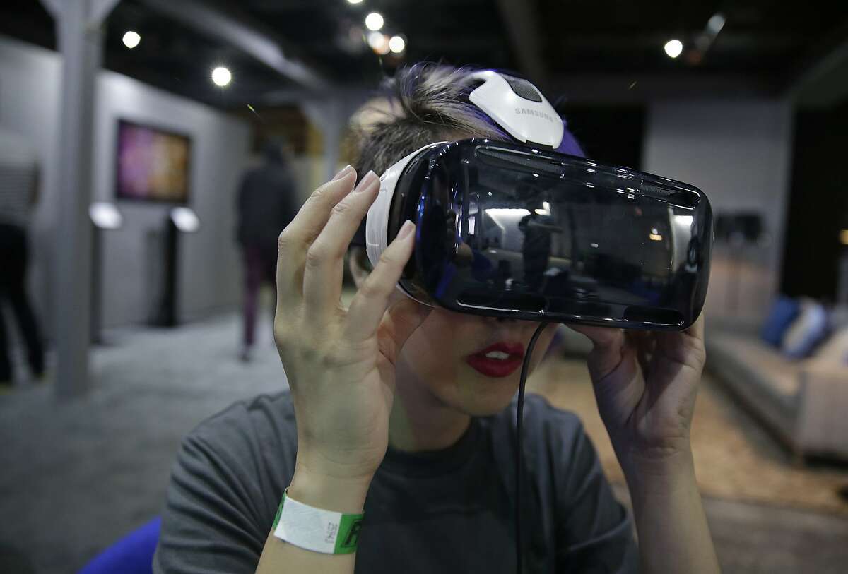 In this March 26, 2015 photo, a woman demonstrates the Oculus virtual reality headset at the Facebook F8 Developers Conference in San Francisco. Once seen as mainly a tool for alien-blasting video gamers, now major movie studios, television producers and even budding artists are adopting the technology that has users donning bulky goggles, entering house-sized domes, even rigging their smartphones to immerse themselves in faraway realms. (AP Photo/Eric Risberg)
