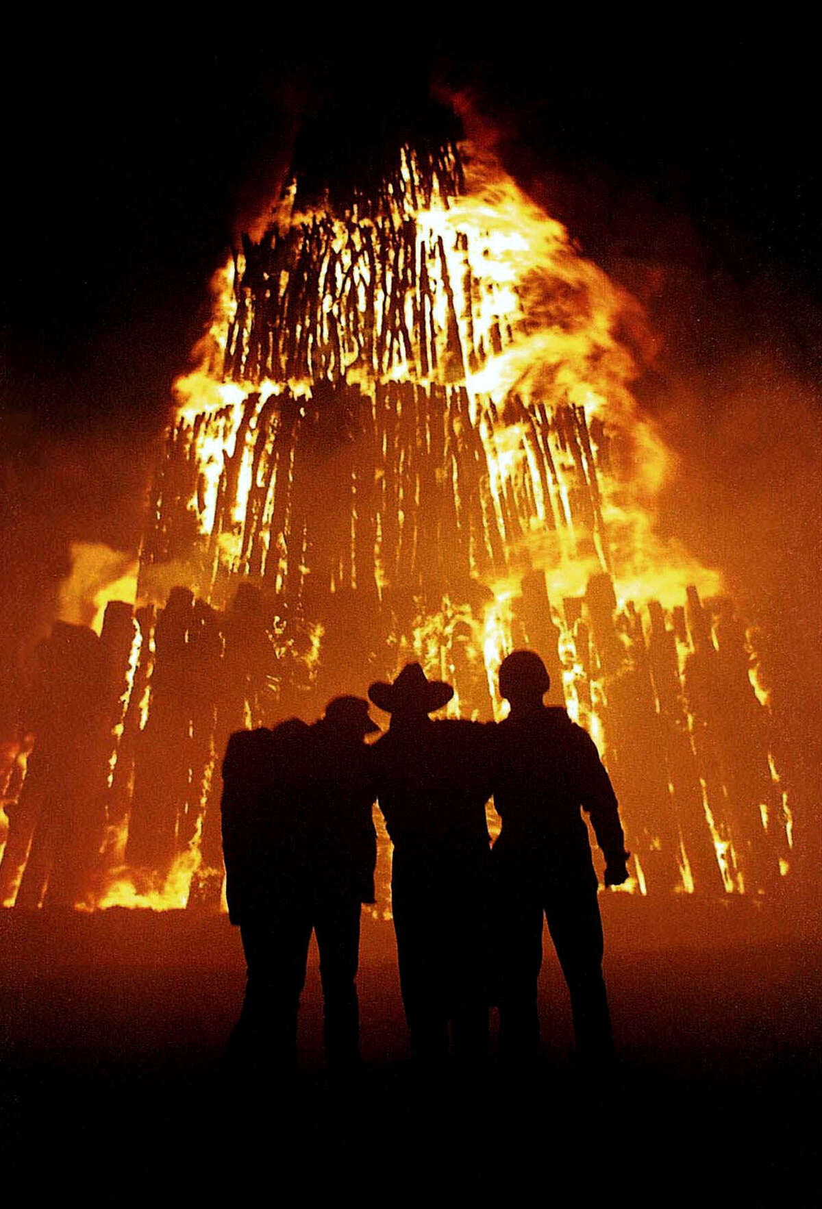 Texas A&M students huddle in front of a bonfire on Nov. 26, 1996, in College Station. At a university steeped in tradition, the burning of bonfire on the night before the annual football game against archrival Texas remains the most hallowed ritual at Texas A&M. But since the stack of more than 5,000 logs collapsed on Nov. 18, 1999, killing 12 Aggies and injuring 27 others, the 90-year-old tradition has been on hold and its future remains in doubt.