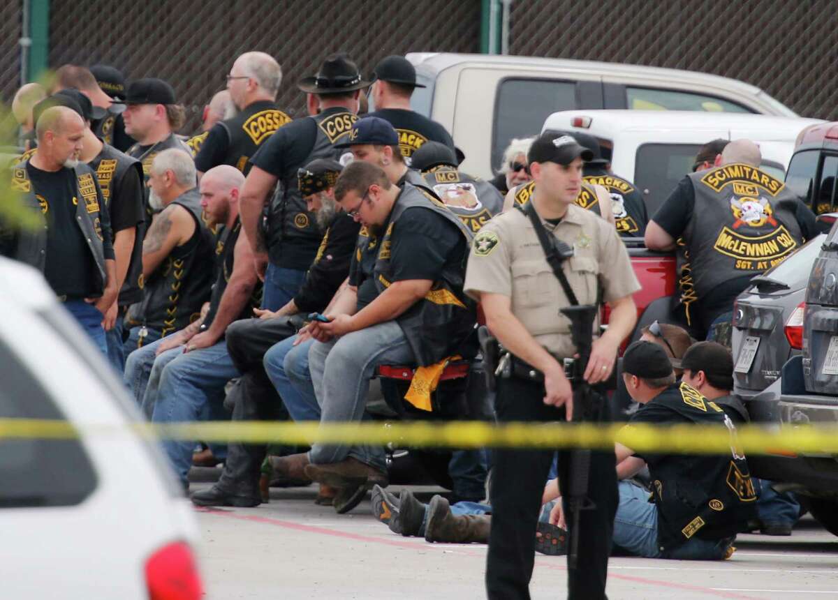 FILE - In this May 17, 2015 file photo, a McLennan County deputy stands guard near a group of bikers in the parking lot of a Twin Peaks restaurant in Waco, Texas. The prevailing images of protests in Baltimore and Ferguson, Missouri, over police killings of black men were of police in riot gear, handcuffed protesters, tear gas and mass arrests. The main images of a fatal gun battle between armed bikers and police in Waco, Texas, also showed mass arrests _ carried out by nonchalant-looking officers sitting around calm bikers on cell phones. (Rod Aydelotte/Waco Tribune-Herald via AP)