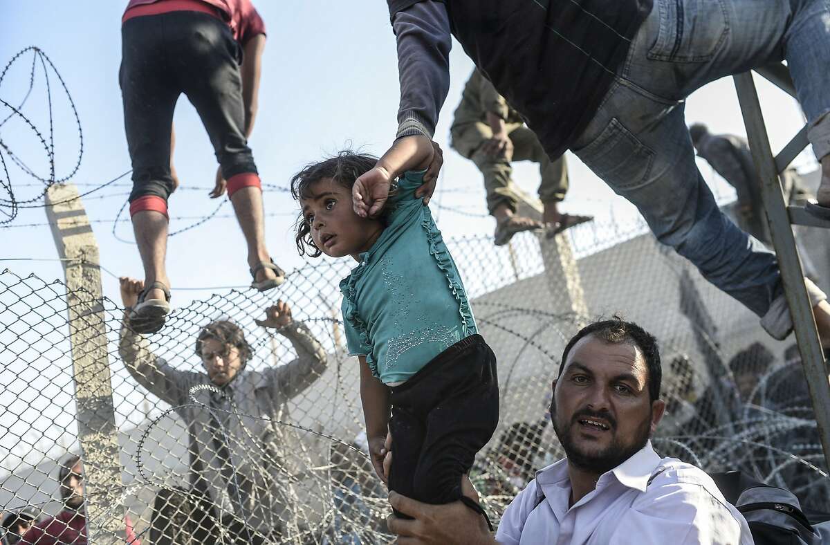 A Syrian child fleeing the war is lifted over border fences to enter Turkish territory illegally, near the Turkish border crossing at Akcakale in Sanliurfa province on June 14, 2015. Turkey said it was taking measures to limit the flow of Syrian refugees onto its territory after an influx of thousands more over the last days due to fighting between Kurds and jihadists. Under an "open-door" policy, Turkey has taken in 1.8 million Syrian refugees since the conflict in Syria erupted in 2011. 