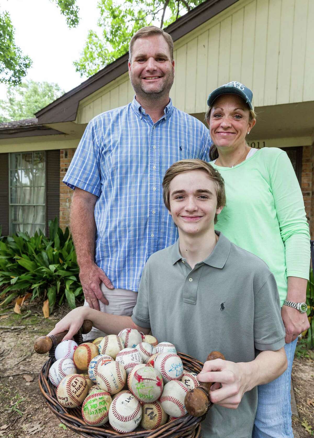 14-year-old (Monday 6-15-15 is his 14th birthday) Walker Johnson was hit in the chest by a baseball in April. His heart stopped but he was revived and he will throw out the first pitch at Monday's Astro's game. Walker is holding and flanked by dozens of signed "get well" baseballs that have been left at his home in west Houston. L-R ID: Dad Carey Johnson; Walker Johnson, 14; mom Christy Johnson. Sunday June 14, 2015