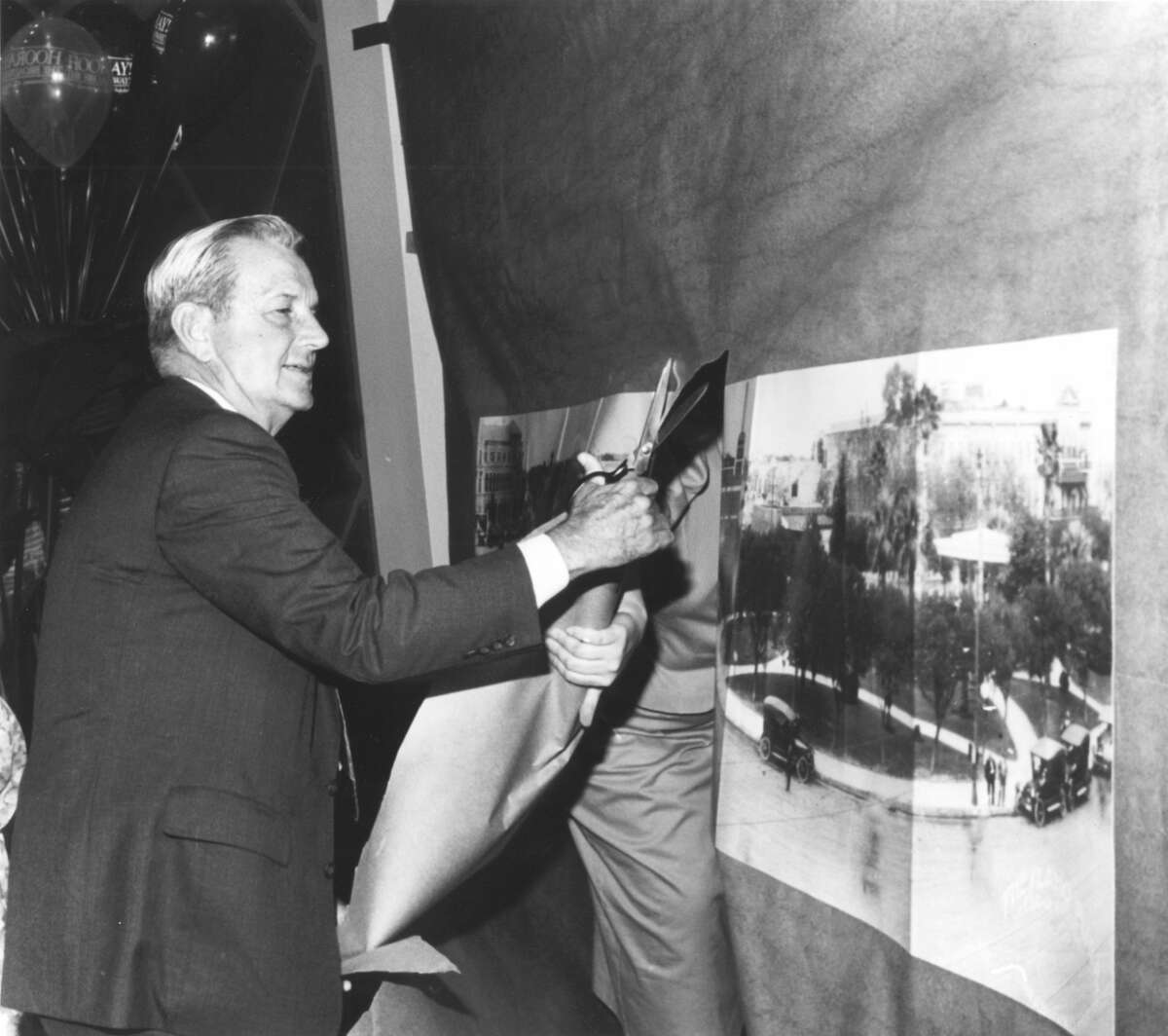 Charles B. Cheever Jr., senior chairman of the Broadway National Bank, cuts through a copy of a panoramic picture of Alamo Plaza that was taken by the late E. O. Goldbeck, to open the new branch of the bank in the downtown area.