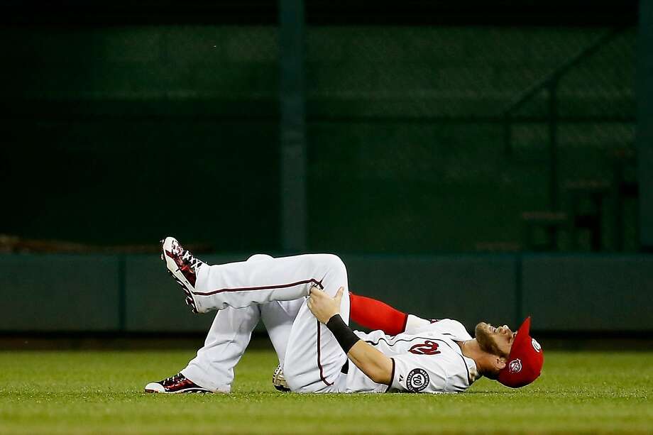 bryce harper grabs his injured leg after slipping on the wet