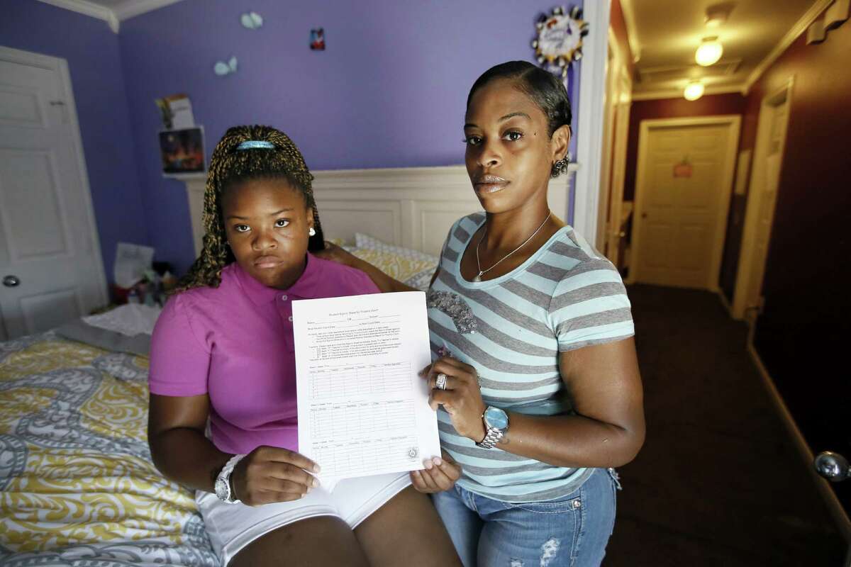 Natod'Ja Washington, left, 16, poses for a photo with her mother Natasha Holloway in their home as they hold a student sign in sheet for truancy court Friday, June 19, 2015, in Dallas. The form must be signed by all of her teachers confirming Washington's attendance in school. (AP Photo/Tony Gutierrez)
