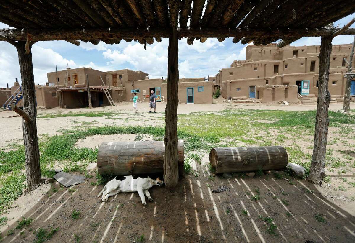A dog naps beneath a wooden canopy at the Taos Pueblo in New Mexico as tourists walk around the North village on Tuesday, June 9, 2015. People of the Tiwa tribe have had descendants living on the site since the late 13th, early 14th century. In 1992, the pueblo was acknowledged as an UNESCO World Heritage Site. Nearly 180,000 visitors a year come to the only living heritage site acknowledged by the world organization. New Mexico has three locations designated by UNESCO. (Kin Man Hui/San Antonio Express-News)