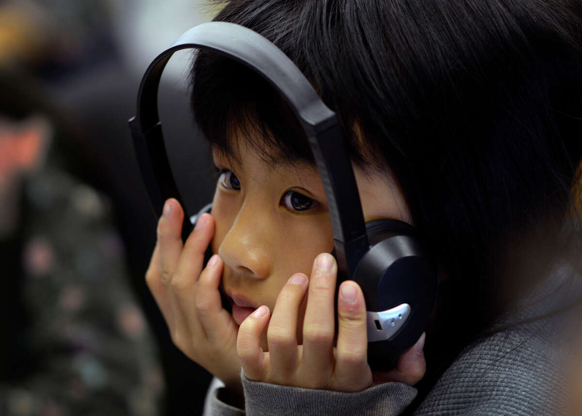 Maureen Wu, 9, holds a pair of headphones to her face as she works inside the TechMobile bus in S.F.