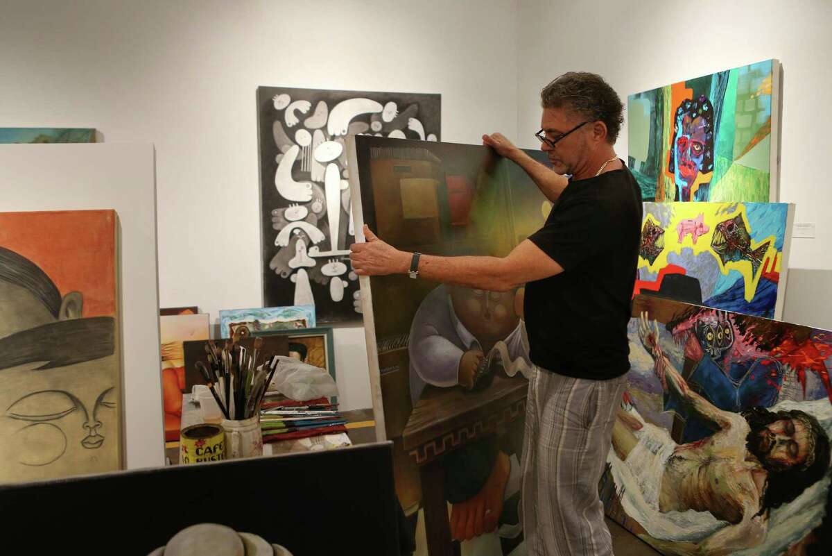 Cuban artist Alberto Godoy holds one of his many pieces of art while standing next to other Cuban artist work that were not able to travel to the united state for their gallery opening on Wednesday, July 1, 2015, in Houston.