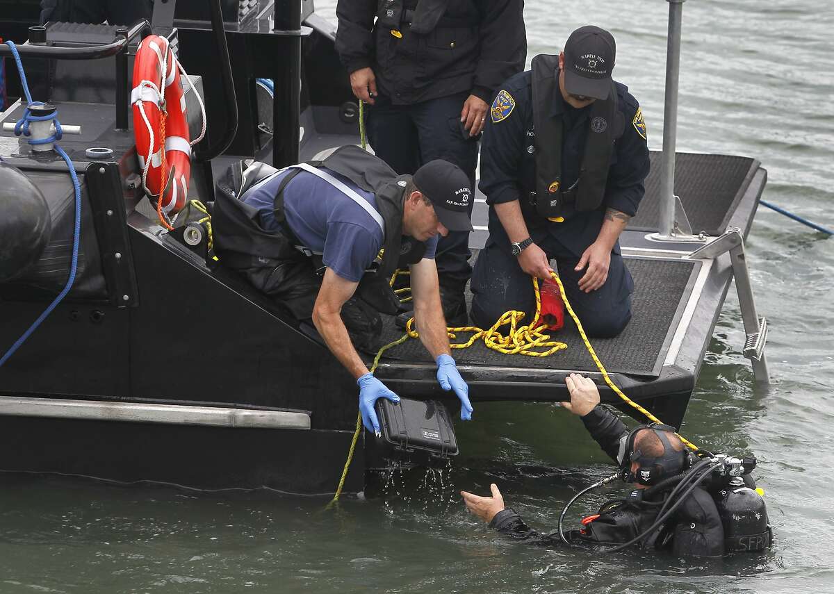 A police department diver hands a box possibly containing evidence found in the bay near Pier 14 to another officer in San Francisco, Calif. on Thursday, July 2, 2015 after a woman was shot and killed walking on the pier with her father yesterday afternoon.