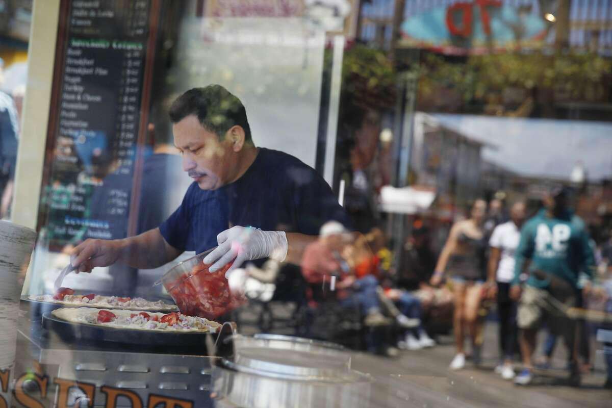 Javier Medina,crepe maker, makes crepes in a window at the Crepe Cafe while visitors at Pier 39 are reflected in the glass of the window on Tuesday, July 7, 2015 in San Francisco, Calif.