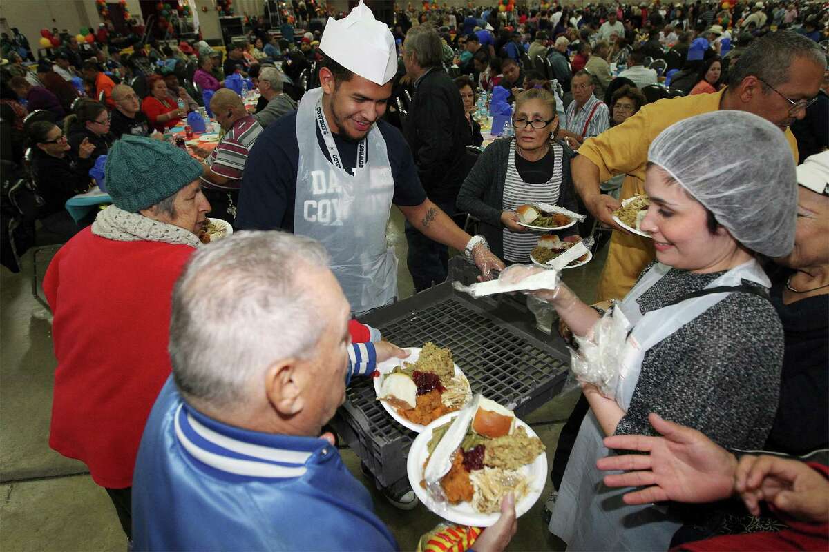 Joshua Guerrero (third from left) and Rocio Portales (right) hand out plates of food to eagerly awaiting guests at the 35th Annual Raul Jimenez Thanksgiving Dinner at the Convention Center on Thursday, Nov. 27, 2014.