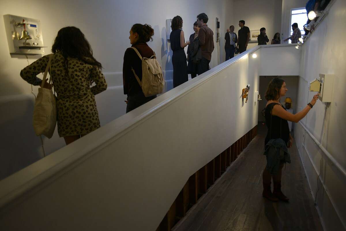Sheena McNeal (right) takes a close look at an art piece by Fernando Orellana while others fill the Incline gallery during the "After Life" art show in San Francisco, California, on Friday, July 10, 2015.