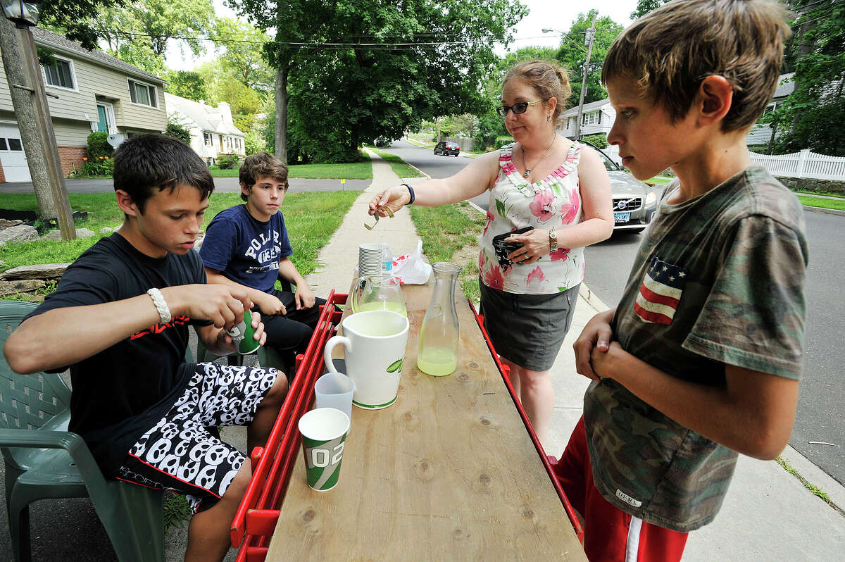 Jack Higgins, left, makes change for Christina Nathanson as Higgins' friends and business partners Nick Palumbo, second from left, and Kristofer Dushi, right, look on at their lemonade stand along Crestview Avenue in Stamford, Conn., on Monday, July 13, 2015. The stand will be open this week from noon to 4 p.m. on Monday, Tuesday, Thursday and Friday. Kristofer is saving money for his mother's birthday, Jack is saving money for a PlayStation 4 and Nick is saving money for a car.