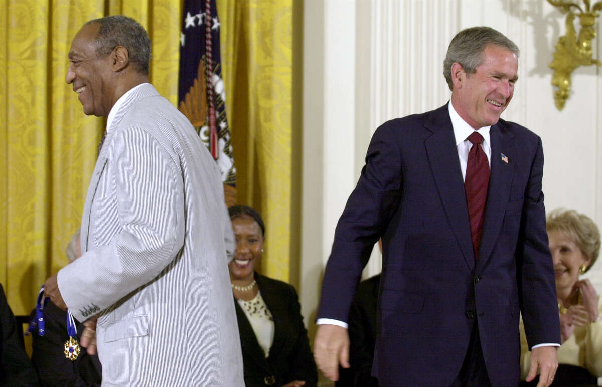 President Bush, right, lets out a laugh after failing to get the clasp together on Bill Cosby's Presidential Medal of Freedom, which Bush tried to put on the entertainer, left, in the East Room of the White House, Tuesday, July 9, 2002, in Washington. Cosby, holding the medal, went back to his seat and immediately put it on himself. (AP Photo/Kenneth Lambert)