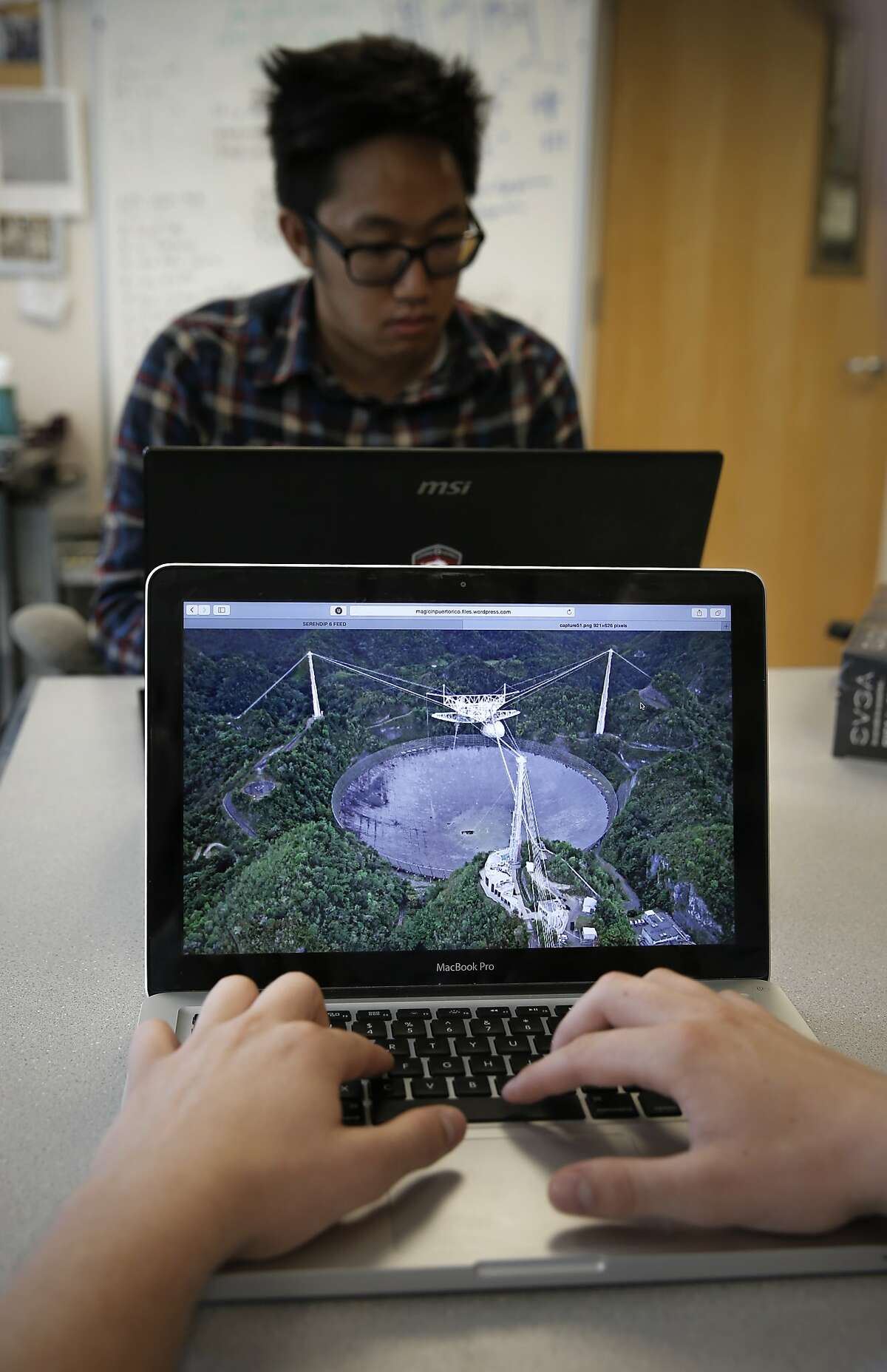UC Berkeley student Kyle Archer, (front) studying mechanical engineering displays a photo of the Arecibo radio telescope in Puerto Rico and Kevin Leong a computer science student at work at the SETI (the Search for Extraterrestrial Intelligence) at Home at the Berkeley SETI research center at UC Berkeley as seen on Fri. July 17, 2015, in Berkley, Calif.