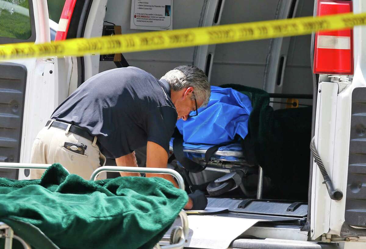 A worker does paperwork near a gurney with a body bag on it in the door of a coroner's van outside of a home in Broken Arrow, Okla., Thursday, July 23, 2015, where five family members were discovered stabbed to death. (AP Photo/Sue Ogrocki)