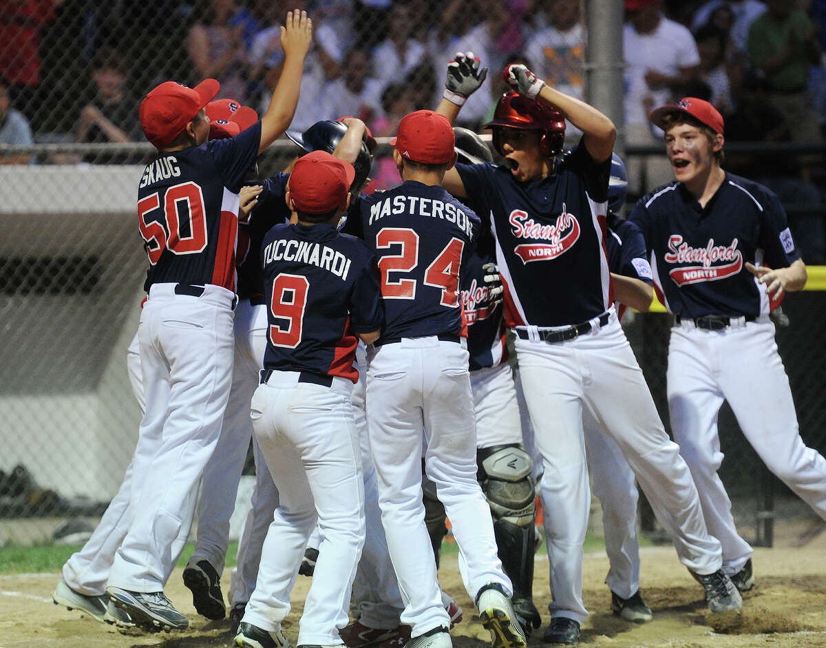 Stamford North's Todd Guttman is mobbed by his teammates as he crosses home plate after clocking a game tying 5th inning home run in the Little League Division 1 championship in Stamford, Conn. on Sunday, July 26, 2015. Stamford North defeated Fairfield American 5-4 in seven innings.
