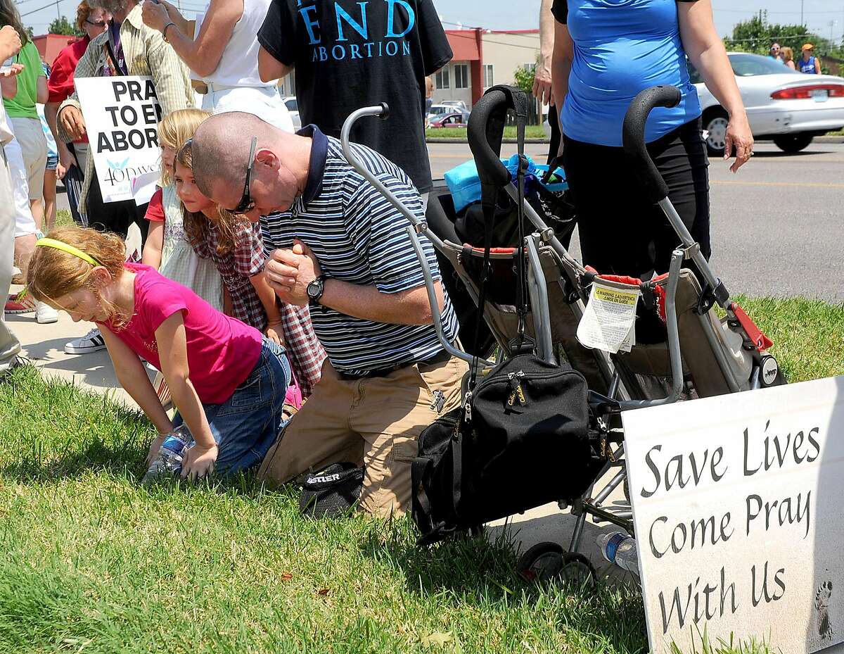 Stephen Smith of Eldon, Mo., prays with his children from left, Gracie, 9, Rachel, 4, and Claire, 6, in front of the Planned Parenthood of Kansas and Mid-Missouri during a rally Tuesday, July 28, 2015, in Columbia, Mo. About forty pro-abortion rights supporters and seventy anti-abortion supporters stood in front of the clinic holding signs as anti-abortion speakers including Mo. Rep. Diane Franklin and Missouri gubernatorial candidate Catherine Hanaway called on state and federal officials to investigate and defund Planned Parenthood. (Don Shrubshell/Columbia Daily Tribune via AP)