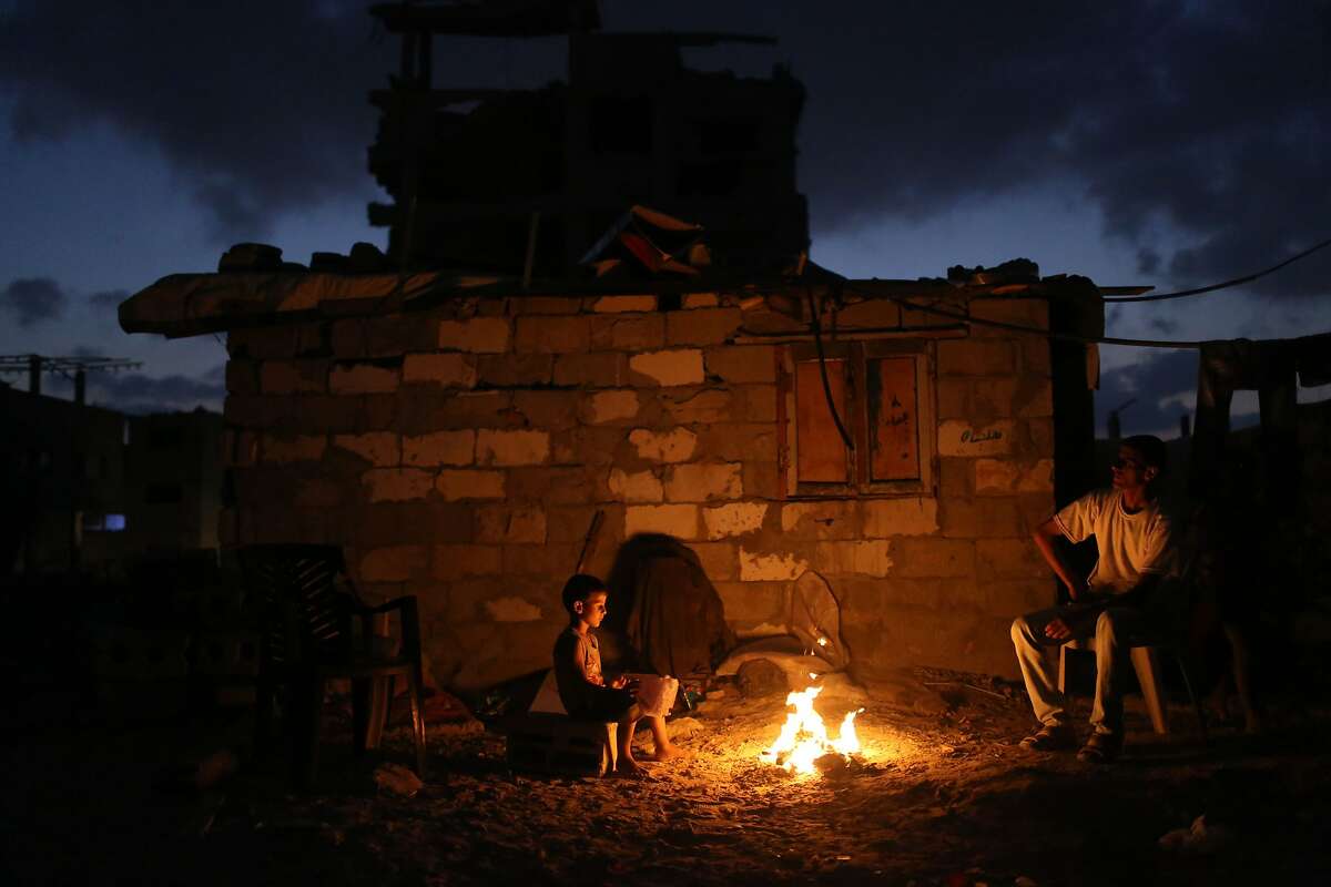 A Palestinian family sits around a fire next to their home in al-Tufah, in the east of Gaza City on July 27, 2015, during a power outage. Residents of Gaza, home to 1.8 million people, have been experiencing up to 15 hours of electricity outage a day for the past two weeks due to fuel and power shortages.