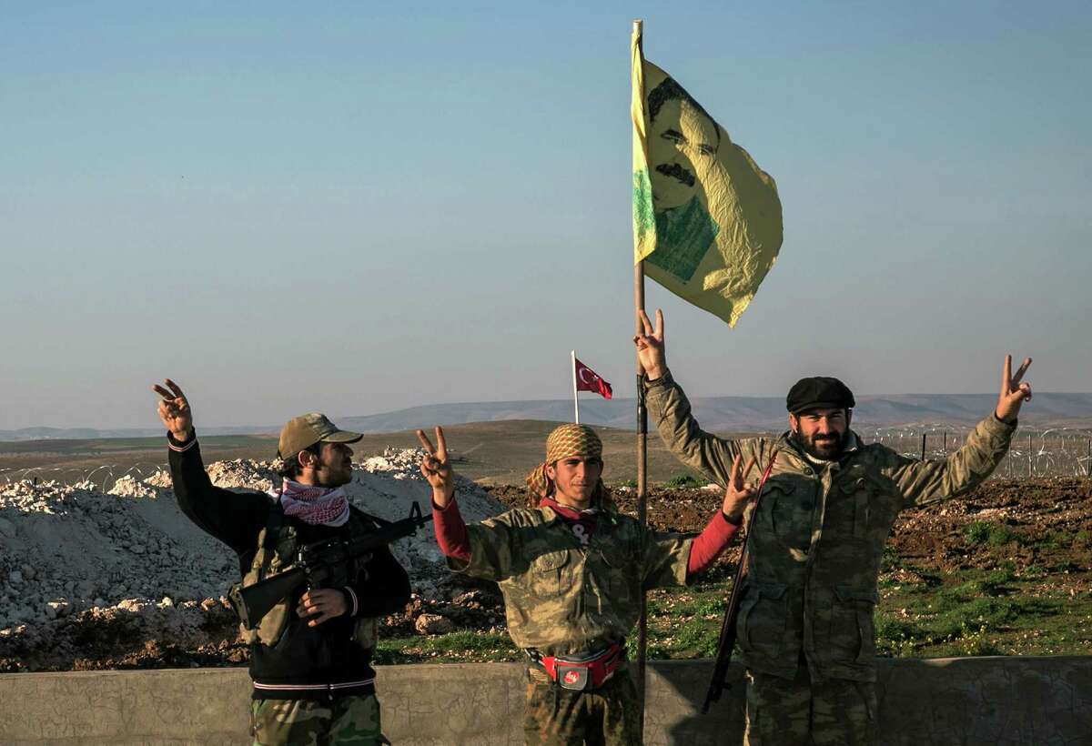 FILE - In this Sunday, Feb. 22, 2015, file photo, Syrian Kurdish militia members of YPG make a V-sign next to poster of Abdullah Ocalan, jailed Kurdish rebel leader, and a Turkish army tank in the background in Esme village in Aleppo province, Syria. Turkish jets struck camps belonging to Kurdish militants in northern Iraq Friday and Saturday in what were the first strikes since a peace deal was announced in 2013. The strikes in Iraq targeted the Kurdistan Workers' Party, or PKK, whose affiliates have been effective in battling the Islamic State group. (AP Photo/Mursel Coban, Depo Photos, File) ORG XMIT: CAIBS102