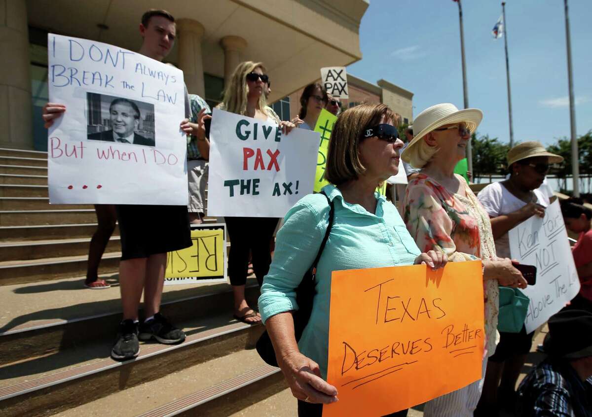 Protesters call for the resignation of Texas Attorney General Ken Paxton as they stand on the Collin County Courthouse steps, Monday, Aug. 3, 2015, in Plano, Texas. Paxton turned himself in Monday to face charges that he misled investors and didn't disclose money he made for referring financial clients as part of his private business before becoming the state's top lawyer in January. (AP Photo/Tony Gutierrez)