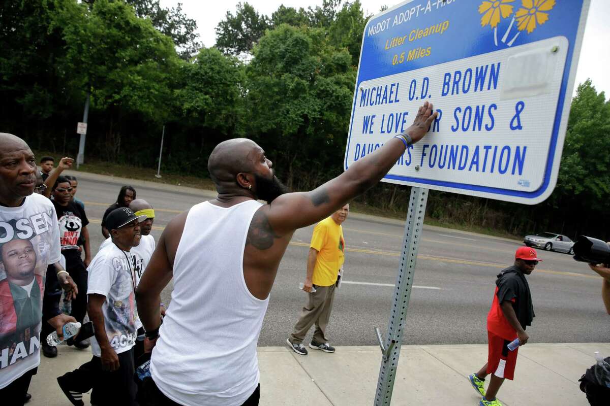 Michael Brown Sr. stops to touch an adopt-a-highway sign as he takes part in a parade in honor of his son, Michael Brown, Saturday, Aug. 8, 2015, in Jennings, Mo. Sunday will mark one year since Michael Brown was shot and killed by Ferguson police officer Darren Wilson. (AP Photo/Jeff Roberson)