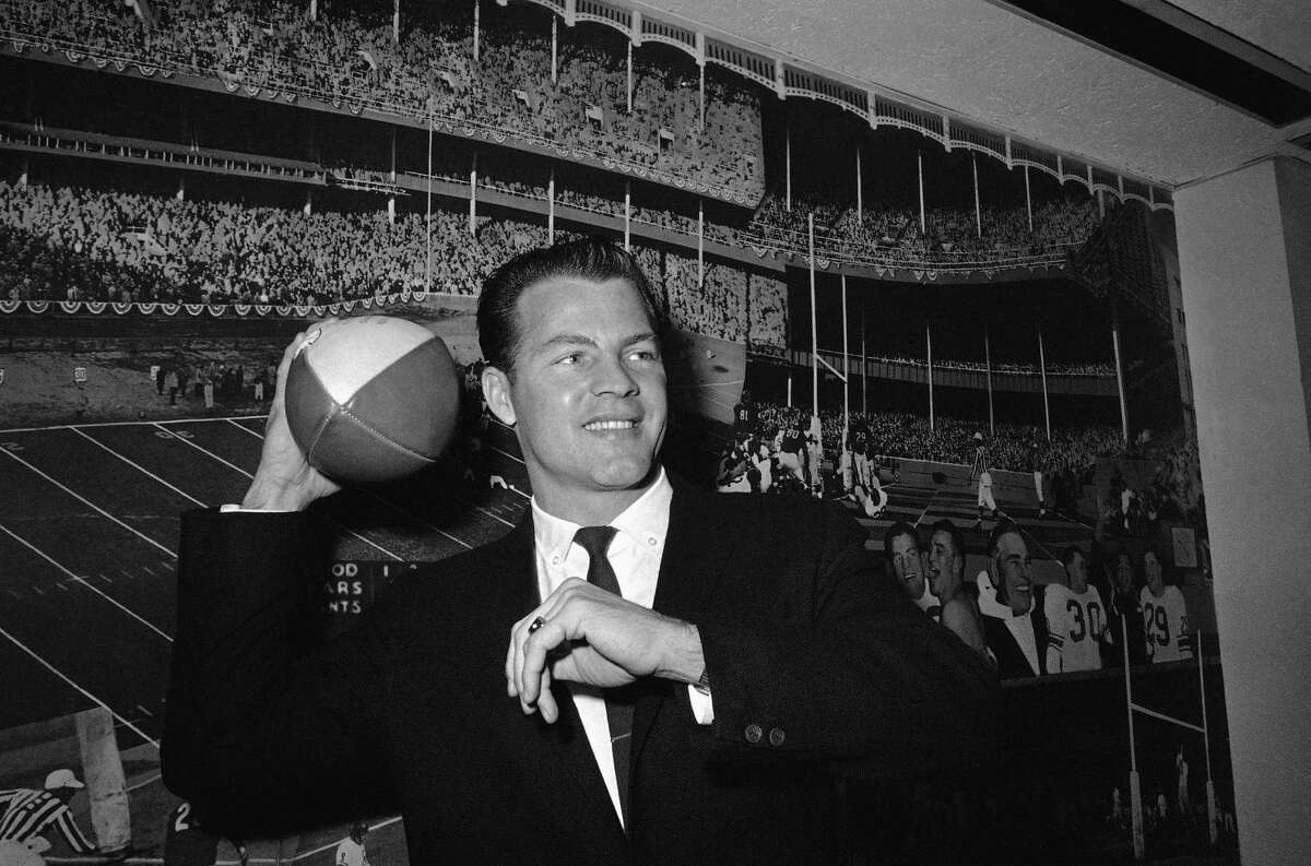 In this April 2, 1962, file photo, New York Giants halfback Frank Gifford cocks his passing arm as he stands in front of photo mural of the Polo Grounds at the offices of the New York Giants in New York’s Coliseum. In a statement released by NBC News on Sunday, his family said Gifford died suddenly at his Connecticut home of natural causes that morning.