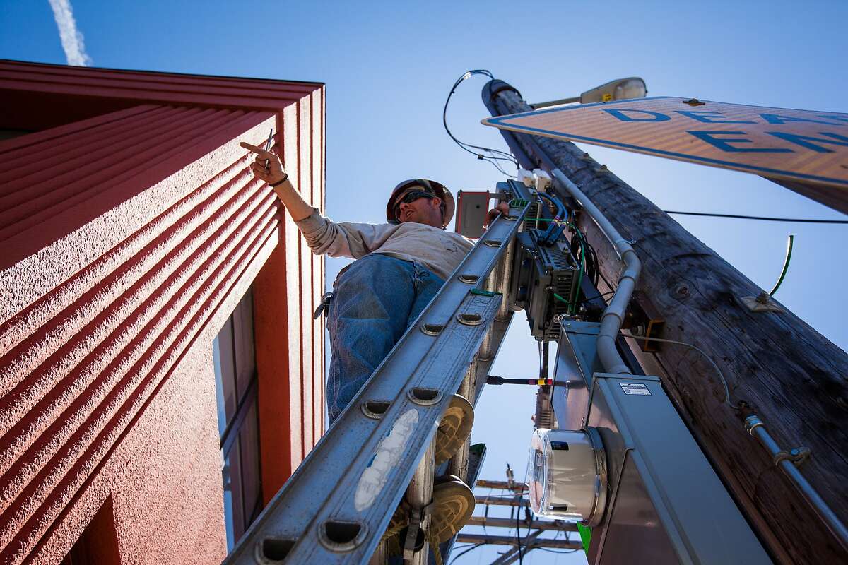Brent Palmer, a contractor with Verizon Wireless, asks one of his crew members for a tool while he installs a remote radio unit (RRU) on a telephone pole in San Francisco, California, on Friday, Aug. 14, 2015. The RRU is a part of the cellular site that transmits the signal to the antenna.