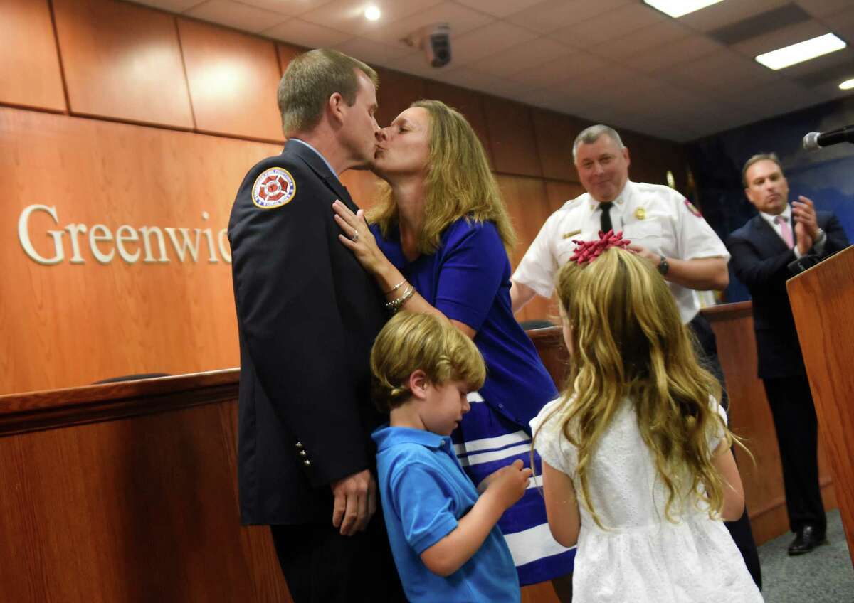 Matthew Brooks kisses his wife, Kristen, as his children, Finn, 5, and Regan, 6, join him up front after being sworn in as a Lieutenant during the Greenwich Fire Department promotional ceremony at Town Hall in Greenwich, Conn. Monday, Aug. 17, 2015. A 10-year veteran, Brooks is a union secretary and instructor who has been working on long-range planning issues in the department.