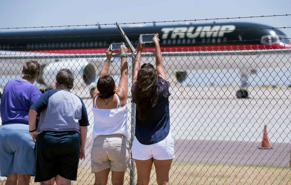 Spectators reach over an airport fence to snap pictures of Donald Trump's plane July 23 at Laredo International Airport. Trump has called for a wall across the entire U.S.-Mexico border.