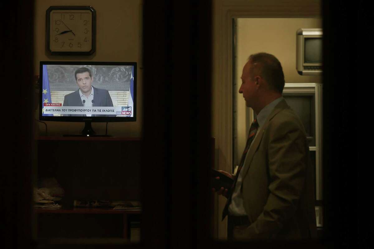 Greek Prime Minister Alexis Tsipras, is seen on a screens during a televised address to the nation, as a policeman of the Greek Presidential Palace looks on, in Athens, Thursday, Aug. 20, 2015. Tsipras announced his governmentâs resignation and called early elections Thursday, seeking to consolidate his mandate to implement a new three-year international bailout that sparked a rebellion within his radical left Syriza party. (AP Photo/Petros Giannakouris)