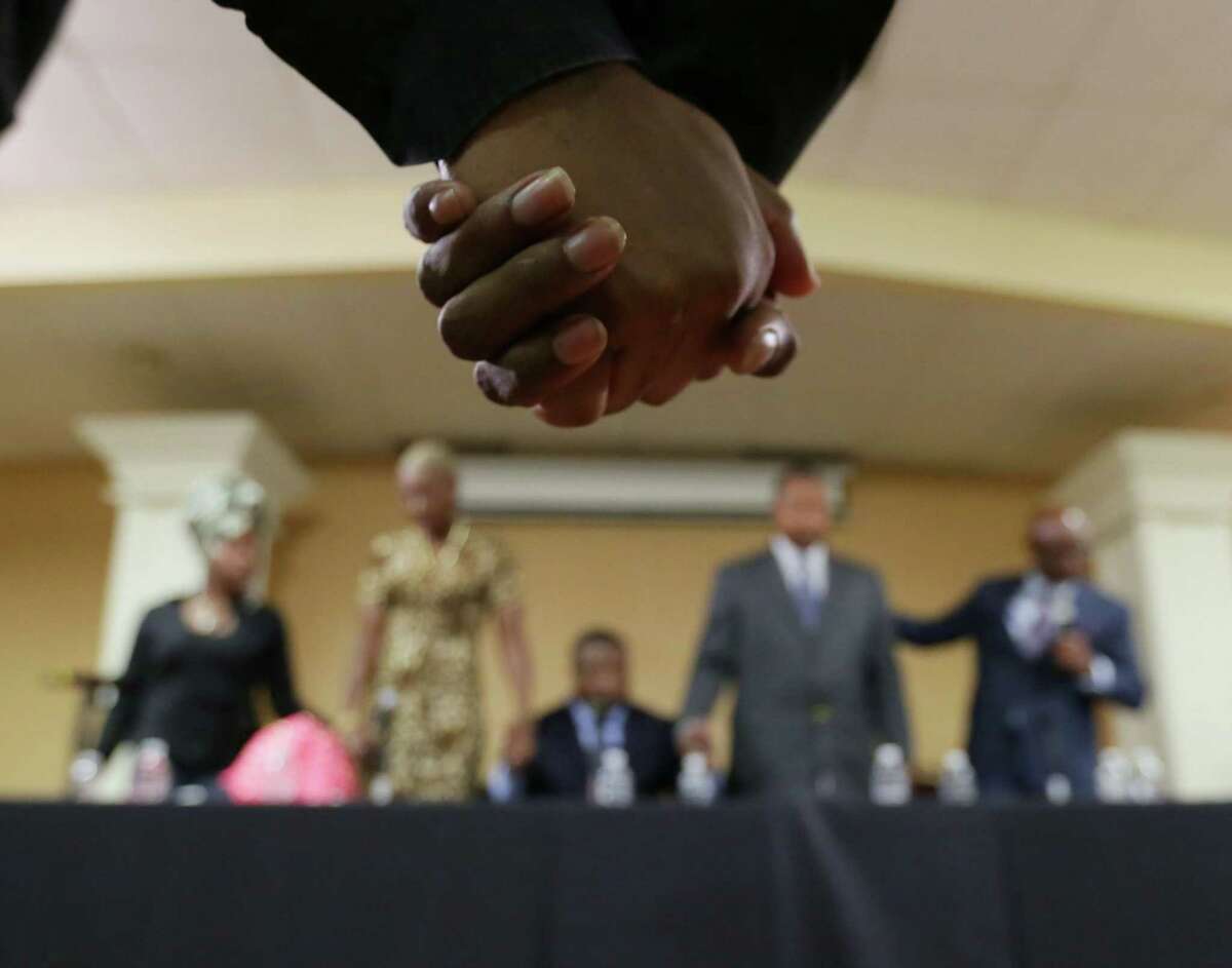 Attendees hold hands as Bishop James Dixon leads a prayer to close a town hall meeting on the conduct of troopers at Community of Faith church on Thursday.