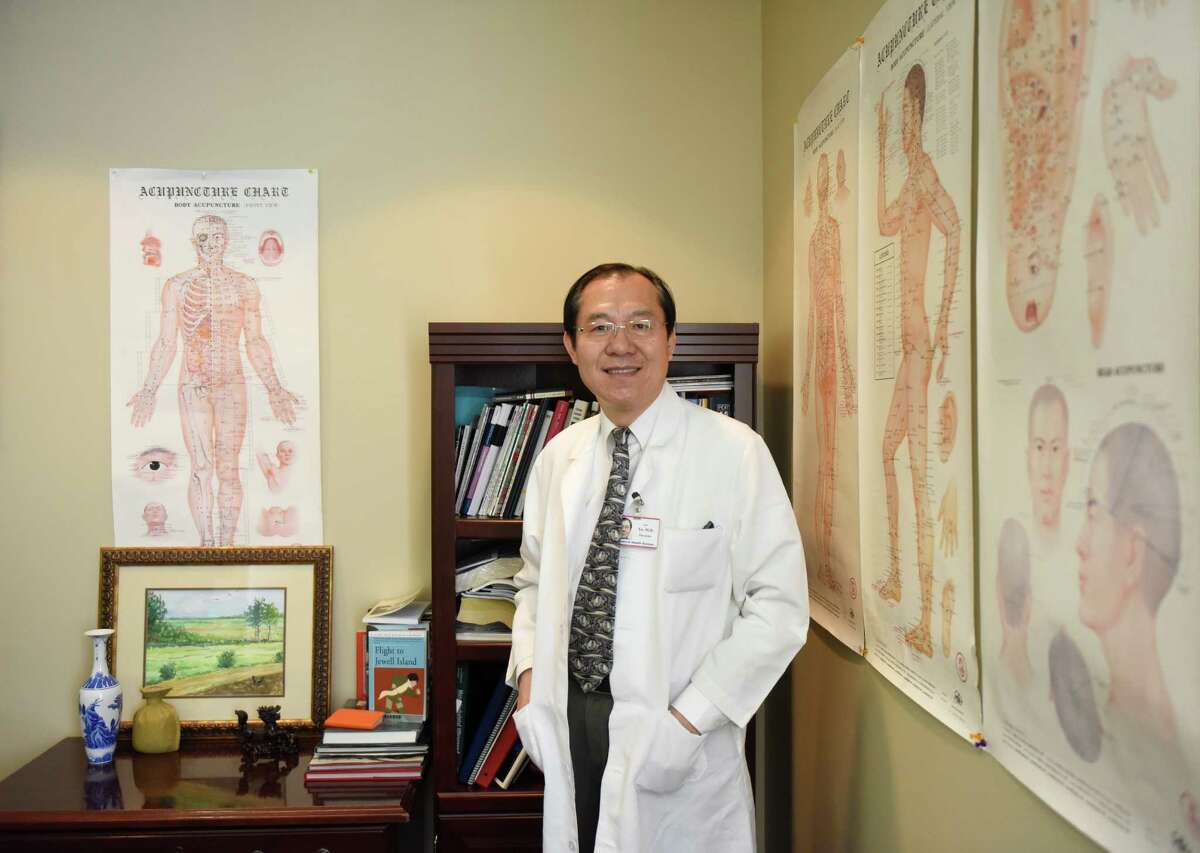 Dr. Jun Xu poses beside acupuncture charts in his office at Rehabilitation Medicine & Acupuncture Center in the Riverside section of Greenwich, Conn. Tuesday, Aug. 25, 2015. Dr. Xu offers acupuncture treatment for infertility, claiming that many patients have been successfully treated.