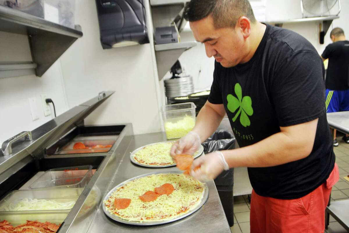 Galo Torres, kitchen manager at the Colony Grill, places pepproni on a pizza.