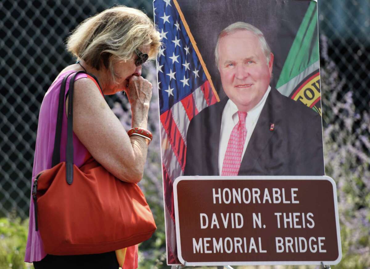 Ginny Theis, sister of Dave Theis, takes a moment after a photograph of Theis and bridge signage are revealed during the bridge renaming ceremony for the late town Selectman David Theis at the Route 1 bridge spanning the Mianus River between the Cos Cob and Riverside sections of Greenwich, Conn. Sunday, Aug. 30, 2015. The bridge was officially renamed The Honorable David N. Theis Memorial Bridge on what would have been Theis' 66th birthday. Theis, who died suddenly last December, worked to put up American flags on the bridge every summer to pay tribute to America and its armed forces.