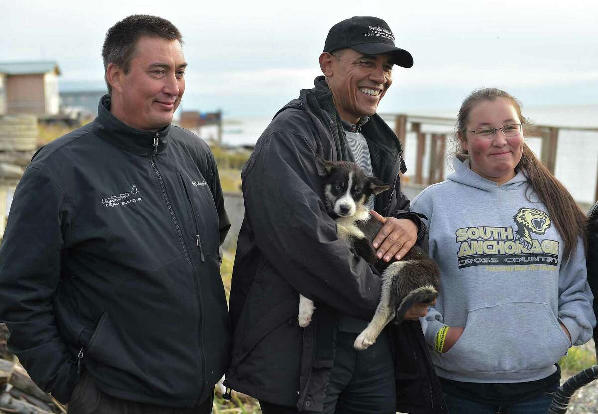 President Barack Obama holds a puppy while posing with a musher in Kotzebue, Alaska. Obama went above the Arctic circle, to urge swift action against climate change, but his positions are based more on politic than science.