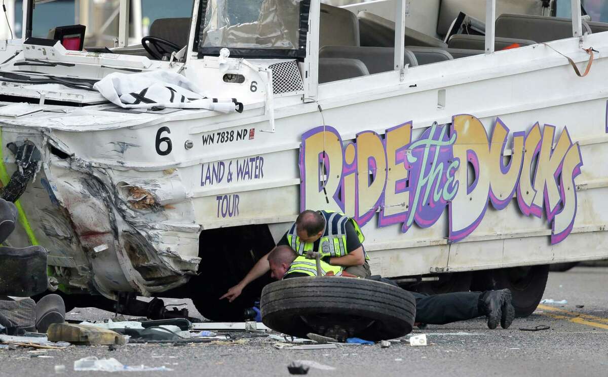 Seattle Police officers look under a "Ride the Ducks" tourist vehicle as a tire and wheel from the bus sits nearby before the bus is loaded onto a flatbed tow truck Thursday, Sept. 24, 2015, after it was involved in a fatal crash with a charter passenger bus earlier in the day in Seattle. (Warning, some graphic content ahead)