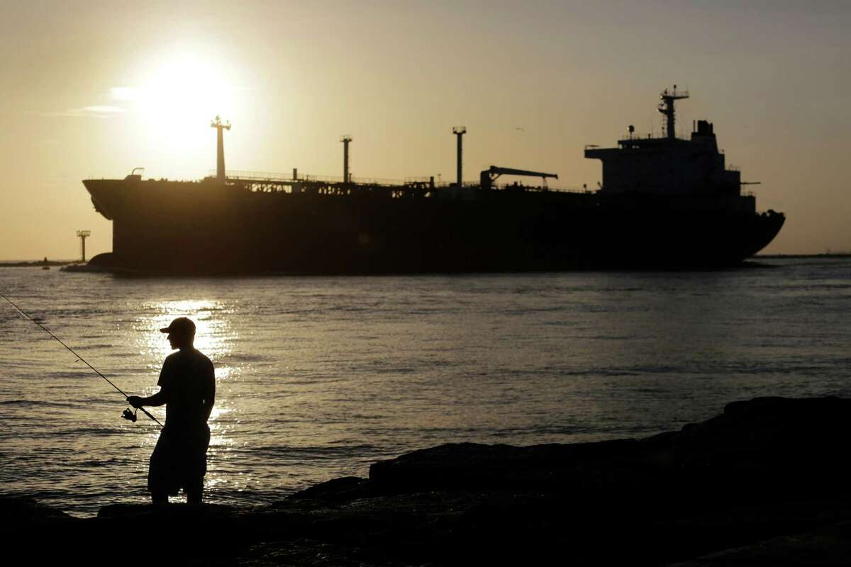 An oil tanker passes a fisherman as it enters a channel near Port Aransas, Texas, heading for the Port of Corpus Christi. The price of oil slid Monday, Aug. 3, 2015, as traders braced for softer demand amid an increase in the number of active crude drilling rigs and weak U.S. economic reports on construction spending and manufacturing activity. (AP Photo/Eric Gay, File)